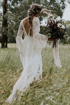 a woman in a wedding dress walking through tall grass with her back to the camera