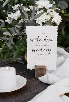 a white sign sitting on top of a wooden table next to a vase with flowers