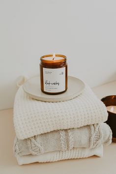 a candle sitting on top of a white plate next to some folded towels and sunglasses