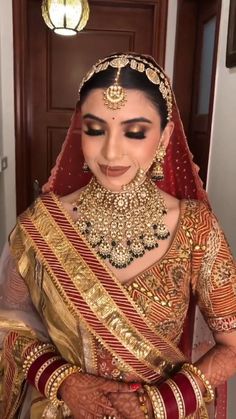 a woman wearing a gold and red bridal outfit with her hands on her chest