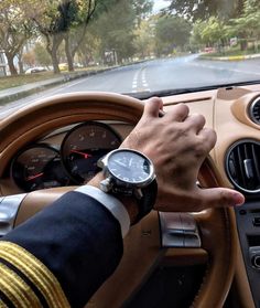 a man driving a car with his hand on the steering wheel while wearing a watch