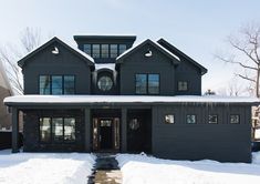 a large gray house with lots of windows and snow on the ground in front of it