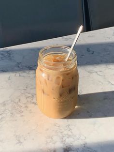 a mason jar filled with iced coffee sitting on top of a marble table next to a window