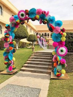 an arch made out of paper flowers on the side of a walkway in front of a building