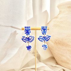 a pair of blue and white earrings sitting on top of a wooden stand next to a curtain