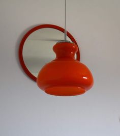 an orange light hanging from a ceiling next to a round mirror on a white wall