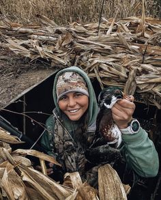 a woman holding a duck in her hand while standing next to a pile of corn stalks