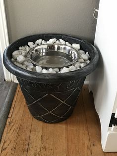 a bowl filled with rocks and water on top of a wooden floor next to a wall