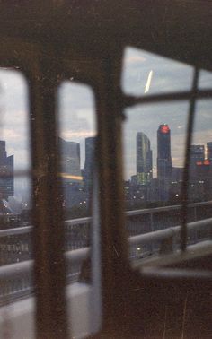 the city skyline seen through two windows in a train car at dusk, as seen from across the tracks