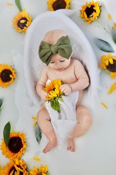 a baby is laying down with sunflowers on the ground and wearing a green bow