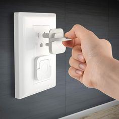 a hand is holding an electrical outlet in front of a wall