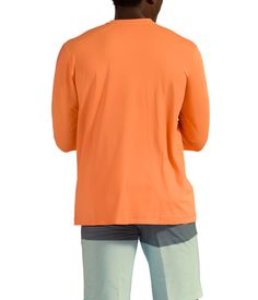 a man in an orange shirt and shorts looking at the back of his head while standing