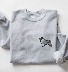 a grey sweatshirt with a dog embroidered on the front and back side, sitting on a white surface