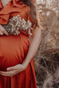 a pregnant woman in an orange dress is holding her belly with flowers on the side