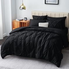 a bed with black comforter and pillows in a bedroom next to a nightstand on a white rug