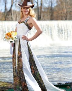 a woman wearing a cowboy hat and dress standing in front of a waterfall with her hands on her hips