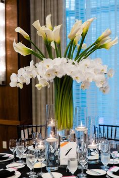 a vase filled with white flowers sitting on top of a table next to wine glasses