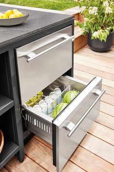 an open drawer in the middle of a table with fruit and water on it next to a potted plant