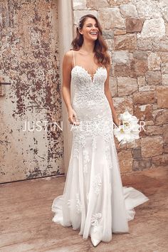 a woman standing in front of a stone wall wearing a white dress and holding a bouquet