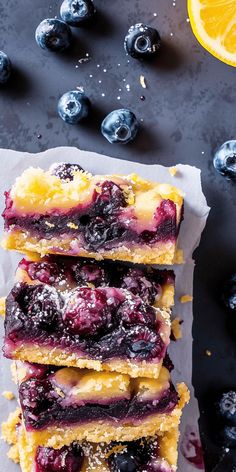 blueberry cheesecake bars stacked on top of each other with lemon wedges next to them