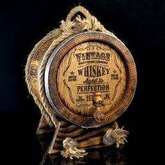 a wooden barrel with rope around it on a black background, the label is whiskey aged to perfection