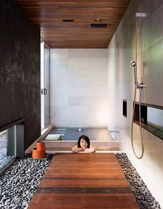 a woman laying in a bathtub next to a wooden floor and wall with rocks