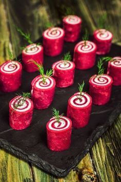 small red rolls with green sprigs on top of them sitting on a black plate