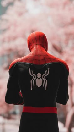 the back view of a spider - man standing in front of a tree with pink flowers