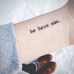 a person with a wrist tattoo that says, be here now