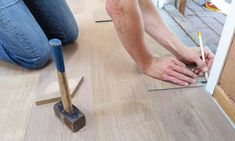 a man laying wood flooring on the ground with a hammer and naildriver