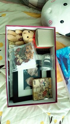 an open box filled with pictures and other items on a bed next to a stuffed animal