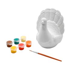 a white ceramic turkey next to some paint and a brush with several different colors on it