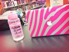 a pink and white laptop sitting on top of a table next to a book shelf