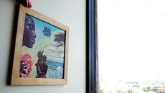 a painting hanging on the side of a wall next to a window with a city view