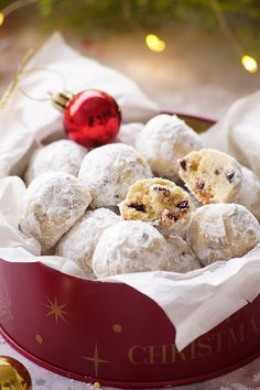 a red bowl filled with snowball cookies next to a christmas tree ornament