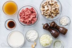 an assortment of ingredients are shown in bowls on a white counter top, including mushrooms, milk, and other foodstuffs