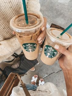 two people holding up starbucks cups with green straws in them and one is holding a brown purse