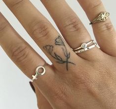 a woman's hand with three rings on it and a butterfly tattoo on the middle finger