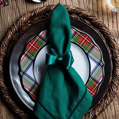 a place setting with green napkins, plaid plates and silverware on a wooden table