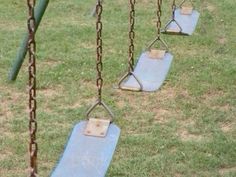 several swings in the grass with chains hanging from them