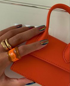 a woman's hand holding an orange purse with two rings on top of it