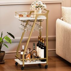 a gold bar cart with wine glasses and bottles on the bottom shelf next to a couch