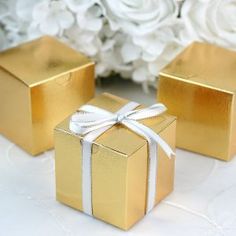 two gold gift boxes tied with white ribbon and sitting next to each other on a table