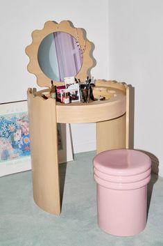 a vanity table with a mirror and a pink trash can on the floor next to it