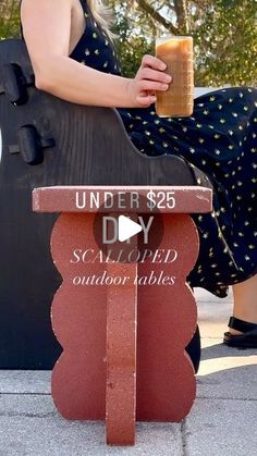 a woman sitting on top of a wooden bench holding a drink in her hand and the words under $ 25 diy scallopped outdoors tables