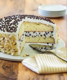 a cake with chocolate chips and white frosting on a plate next to a fork