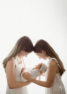 two young women holding a baby in their hands and looking at each other's eyes