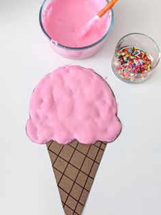 an ice cream cone with sprinkles next to a bowl of pink icing