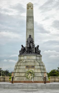 there is a monument that has a wreath on the base and people standing around it