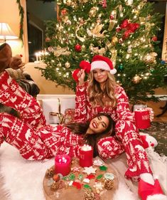 two women in red and white christmas pajamas are laying on the floor next to a christmas tree